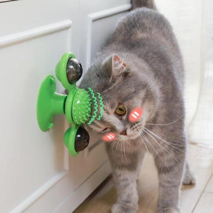 Gray cat rubbing its cheek on a green suction cup windmill cat toy stuck to a white cabinet door