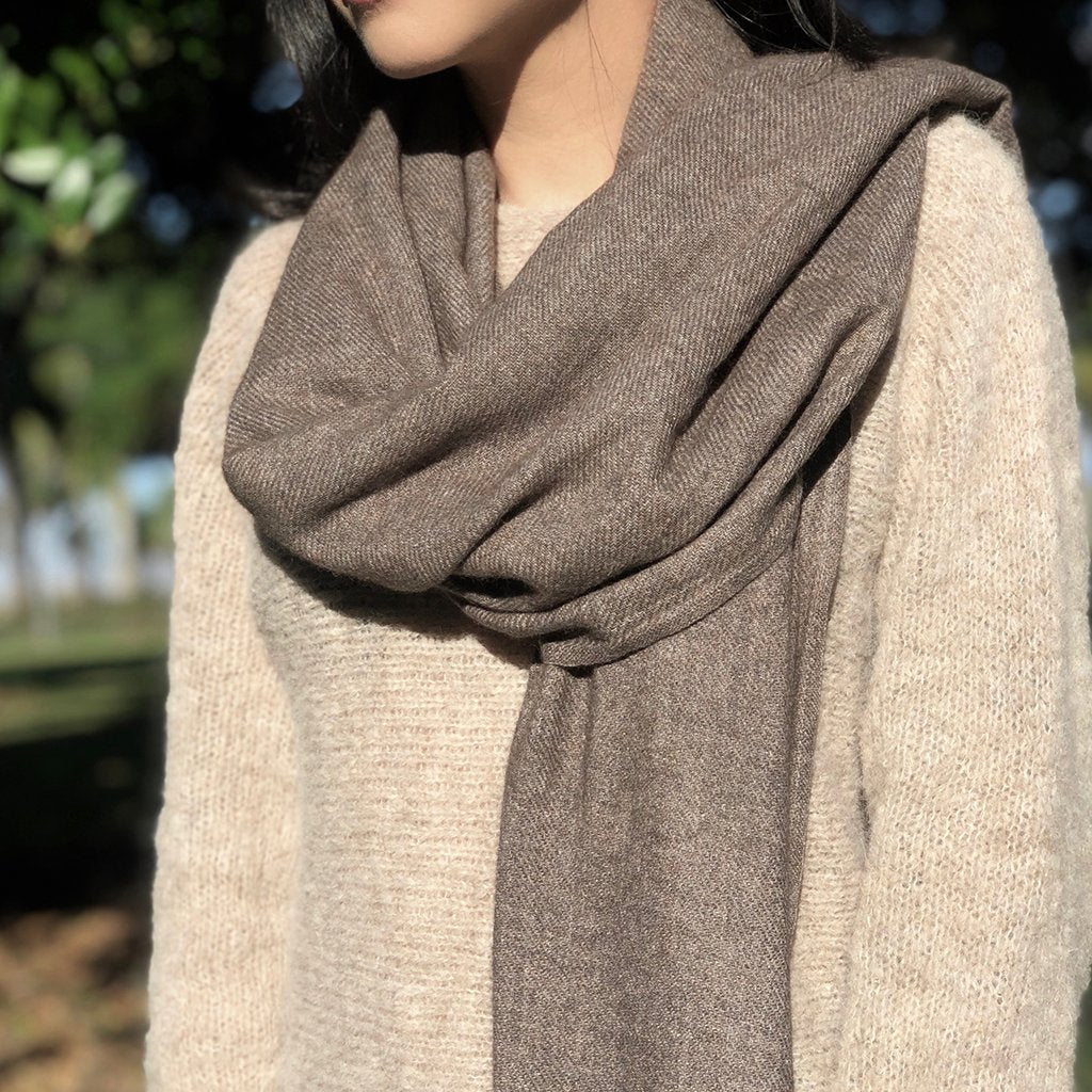 Close view of a woman wearing an espresso brown cashmere scarf looped over a cream knit sweater