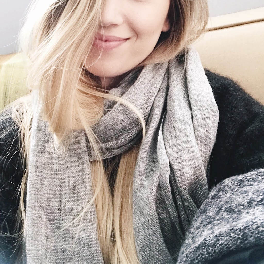 Smiling woman with the gray scarf wound around her neck over a dark coat