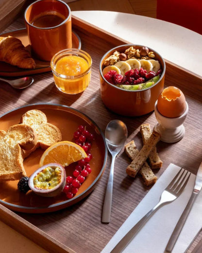 Breakfast tray with a cinnamon plate and matching bowl, fruit, bread and juice.