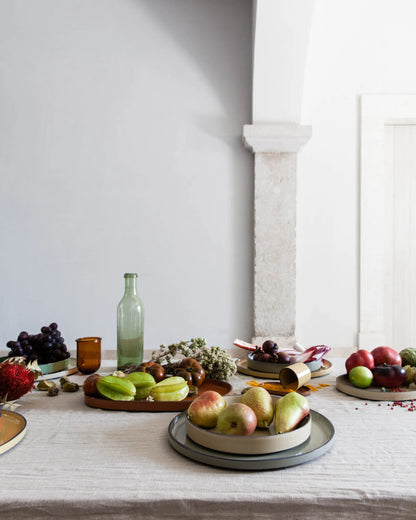 Long laid table with fruit and bottles, a stack of the green glaze plates on it.