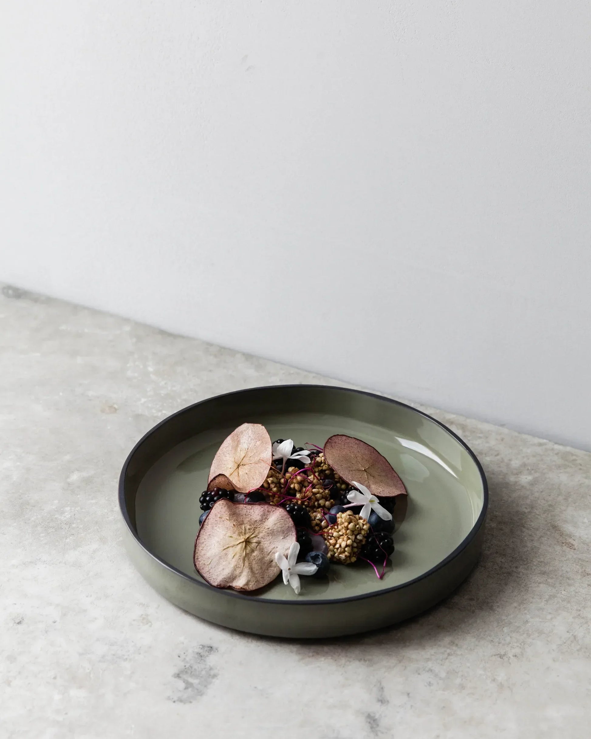 A green glaze deep plate on concrete, plated with meat and a dark garnish.