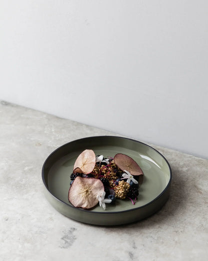 A green glaze deep plate on concrete, plated with meat and a dark garnish.