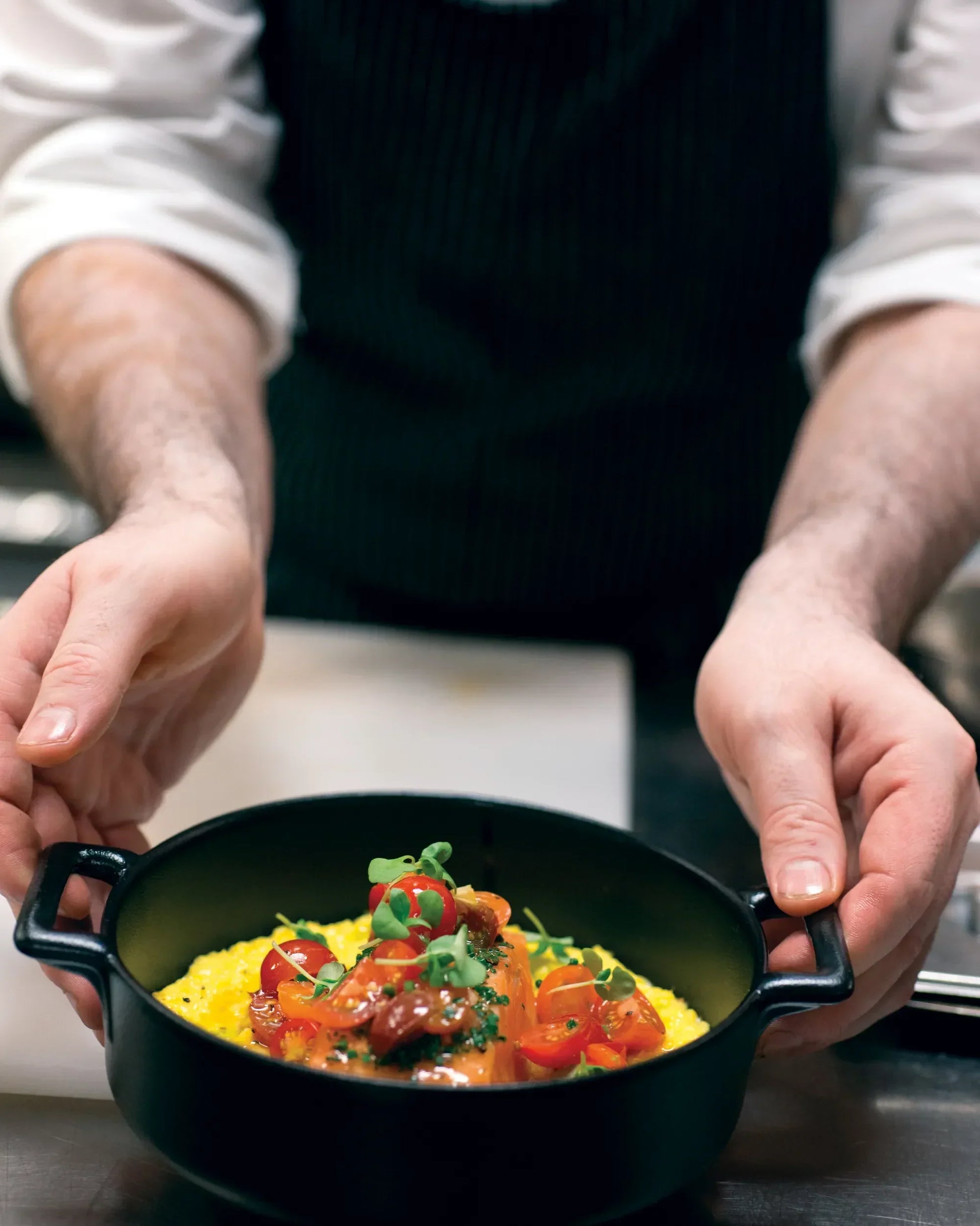 A cook lifting a large black casserole of stew by both of its side handles.