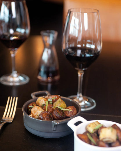 Dark restaurant table with wine glasses, a gray bowl and a small white dish.