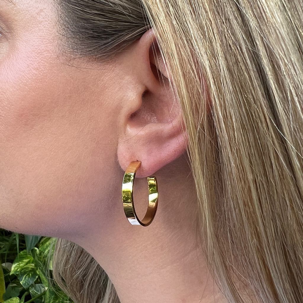 Close view of a chunky gold plated hoop earring worn in the earlobe, framed by blonde hair