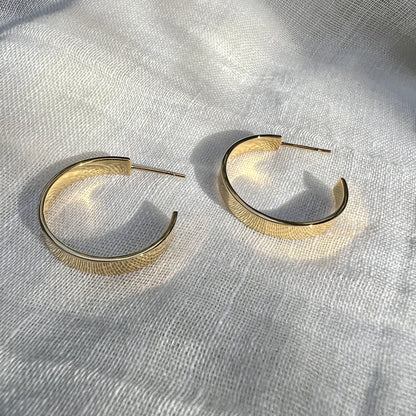 Pair of chunky gold plated hoop earrings on gray linen in bright sunlight