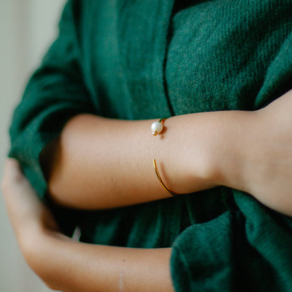 Freshwater pearl bangle worn on a forearm against a dark green knit sleeve