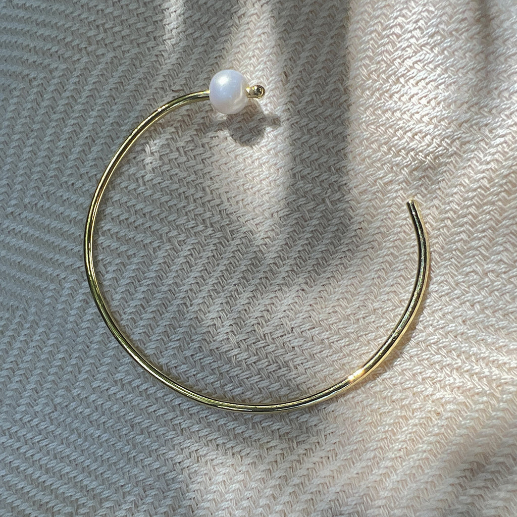 Freshwater pearl bangle lying open on woven cream fabric in soft sunlight
