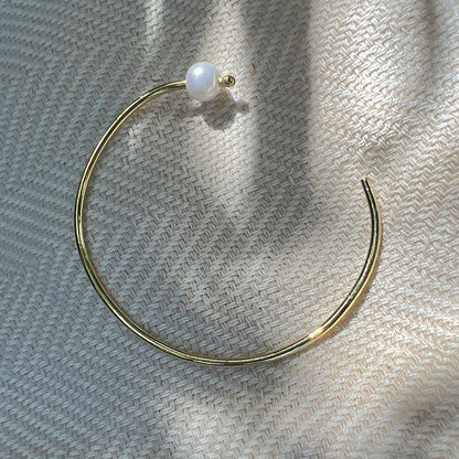 Freshwater pearl bangle lying open on woven cream fabric in soft sunlight