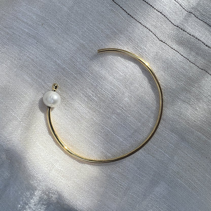 Slim gold plated pearl bangle on gray linen with the pearl tip turned toward the light