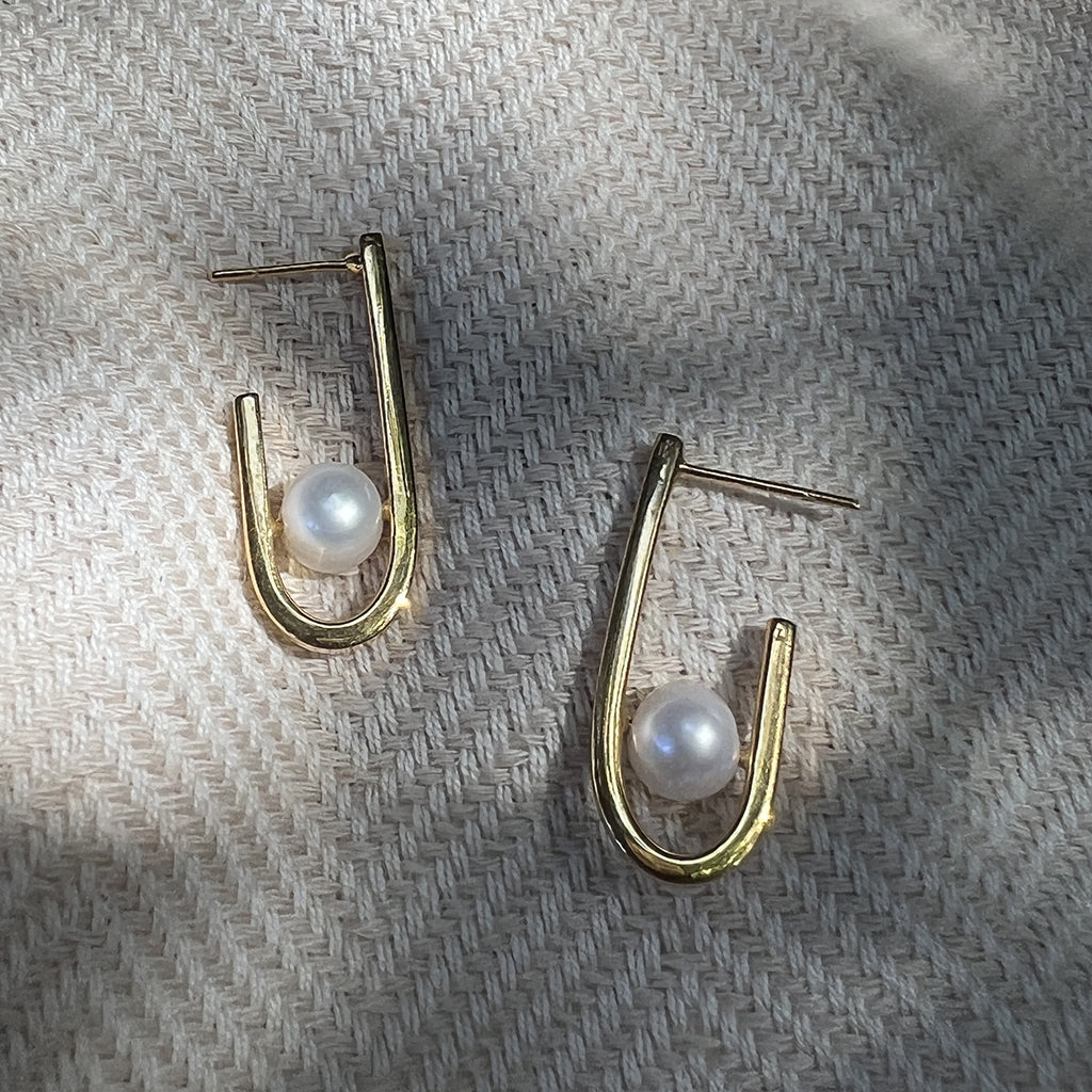 Pair of freshwater pearl J hoop earrings on woven fabric in soft shadow