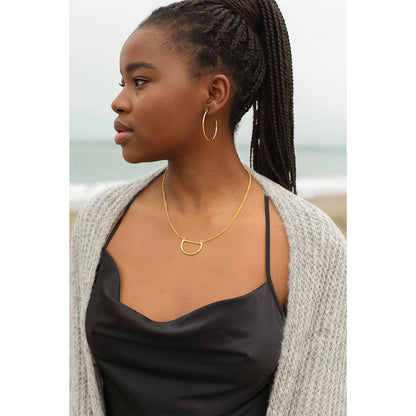 Woman in profile wearing the large gold plated hoop earring with a black slip top and a gray cardigan