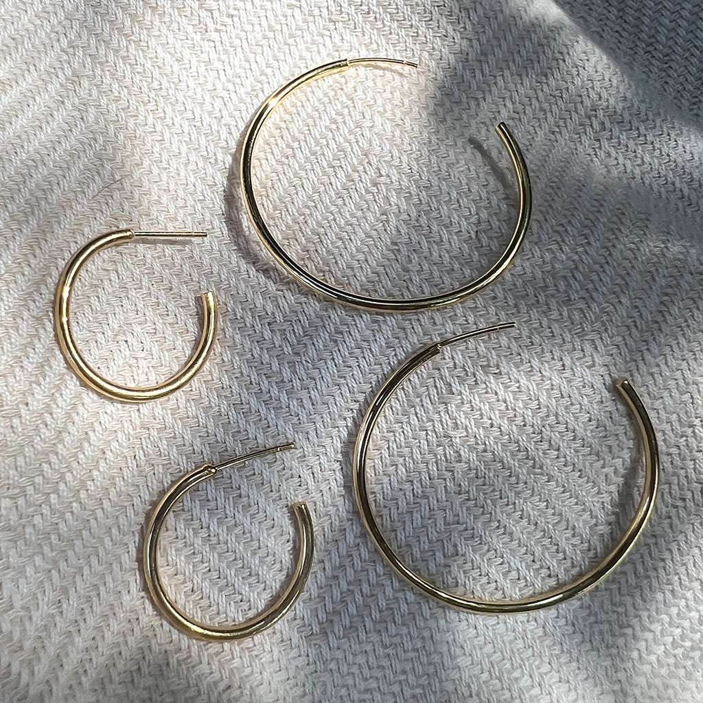 Small and large gold plated hoop earrings laid together on woven linen in sunlight