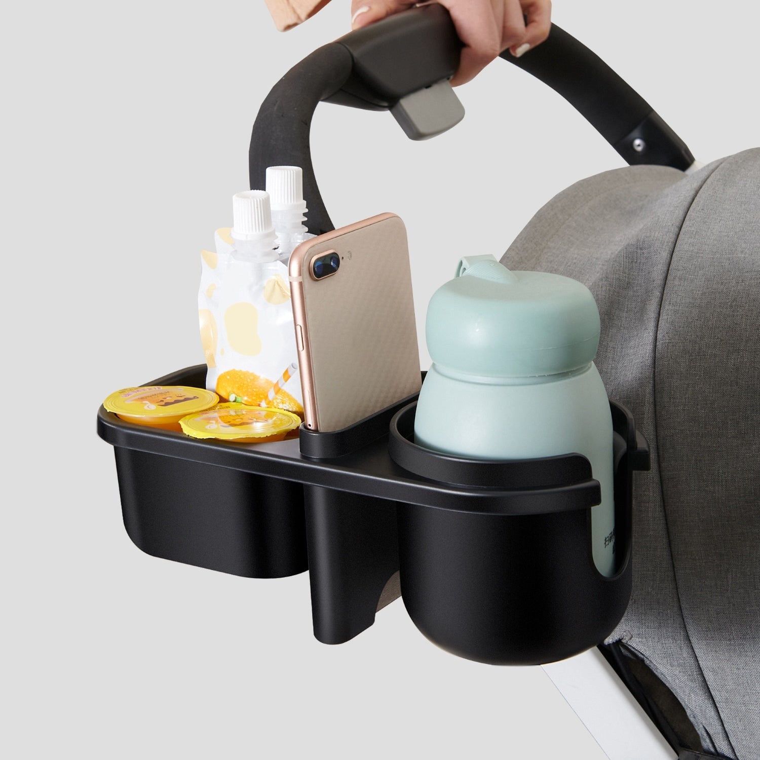 Clamp mounted on a stroller handlebar holding a phone, a snack and a cup.