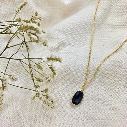 Black quartz pendant necklace on cream fabric beside sprigs of dried white flowers