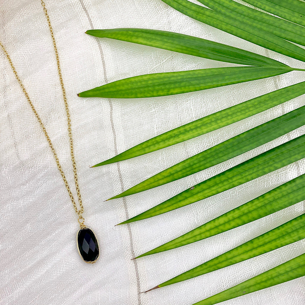 Black quartz pendant necklace on white linen beside a green palm frond