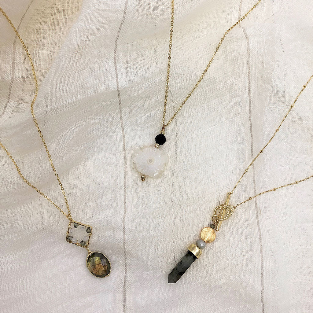 Labradorite lariat with two other stone necklaces laid on striped cream linen