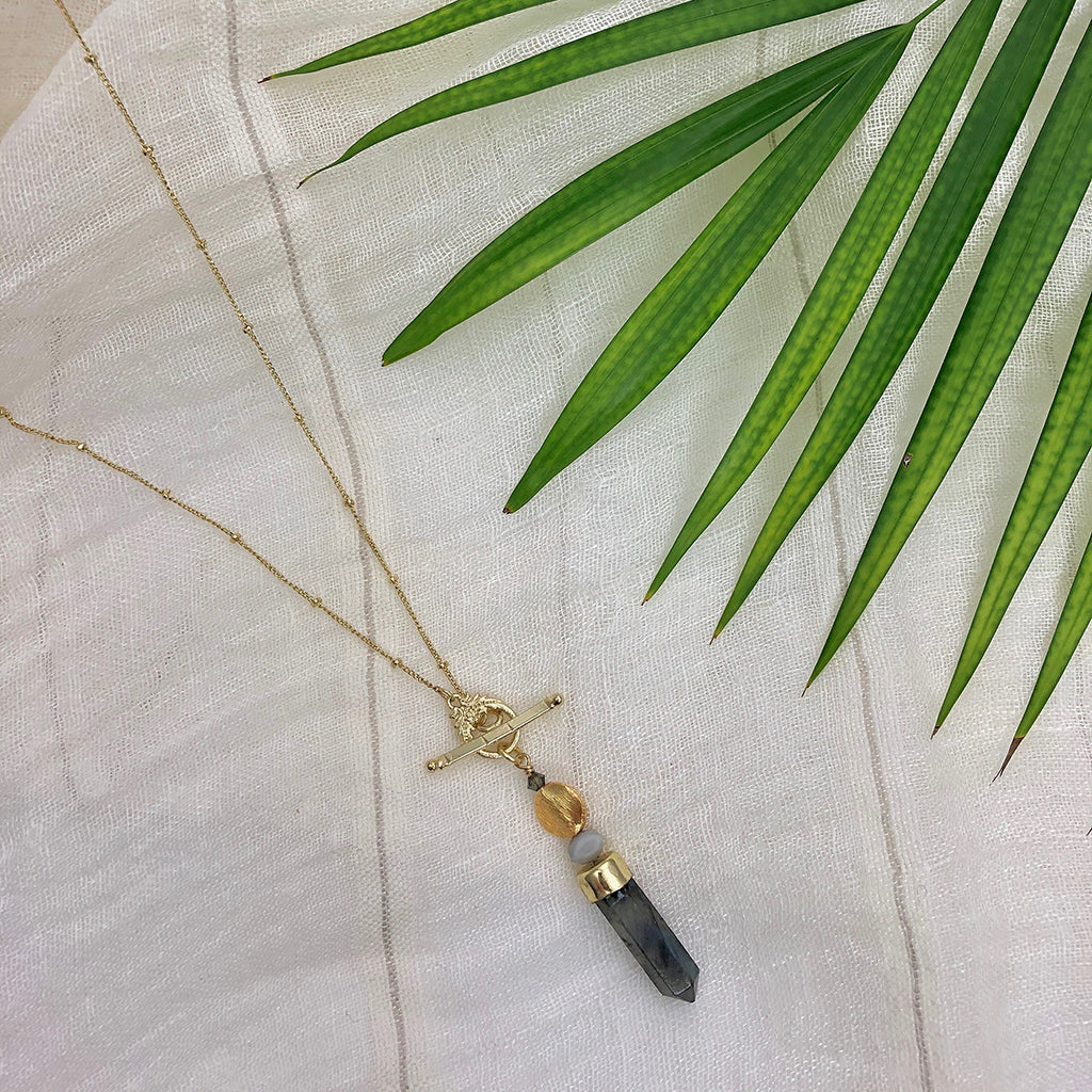 Labradorite lariat necklace on cream linen under a green palm frond