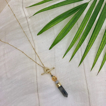 Labradorite lariat necklace on cream linen under a green palm frond