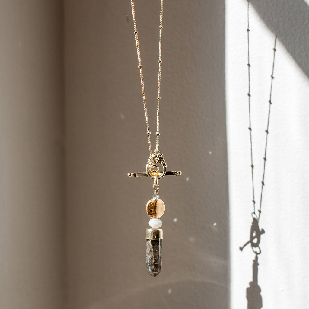 Labradorite lariat necklace hanging in window light with its shadow on the wall