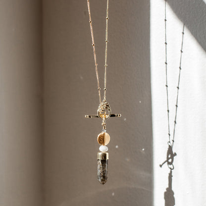 Labradorite lariat necklace hanging in window light with its shadow on the wall