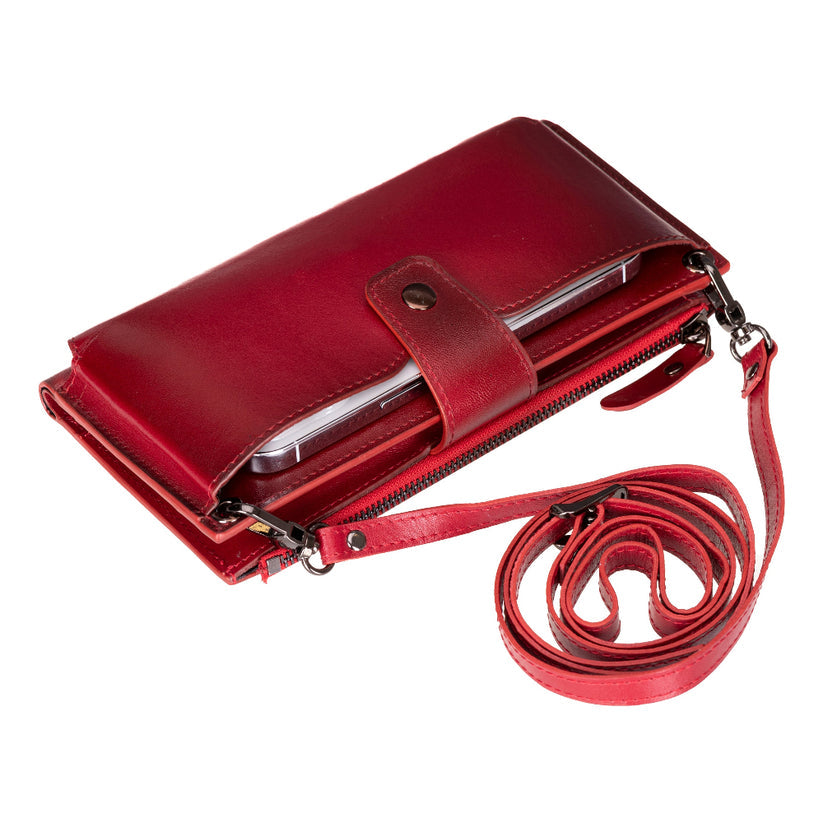 Crossbody phone wallet in Red, a burnished crimson leather, with the strap coiled beside it