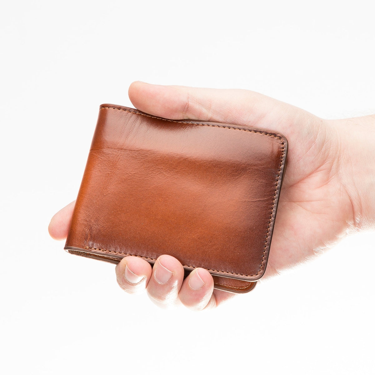 Tan bifold leather wallet held closed in one hand, showing its pocket size