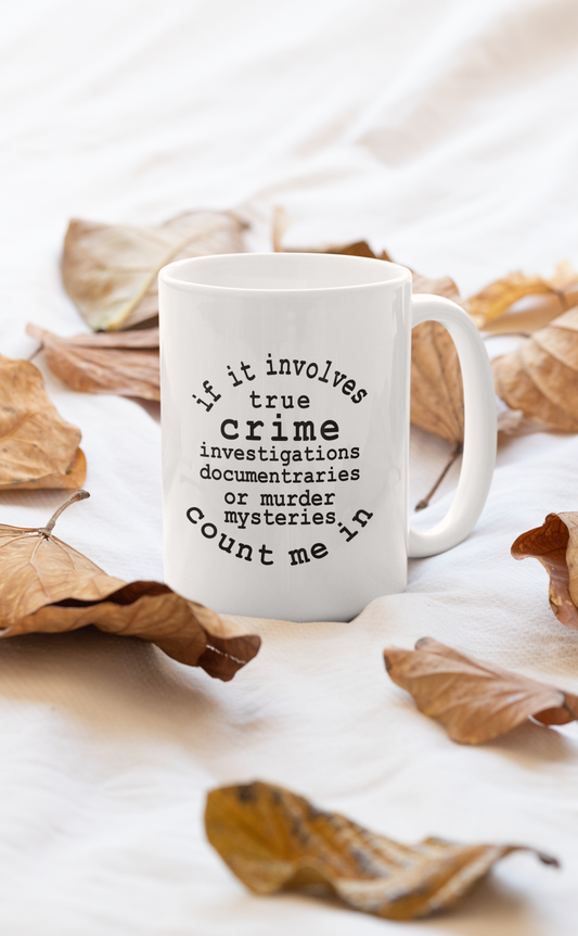 Ceramic 11oz true crime coffee mug surrounded by fall leaves, printed design facing the camera.