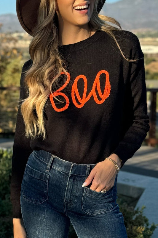 Black knit sweater with orange BOO script, worn with jeans, front view