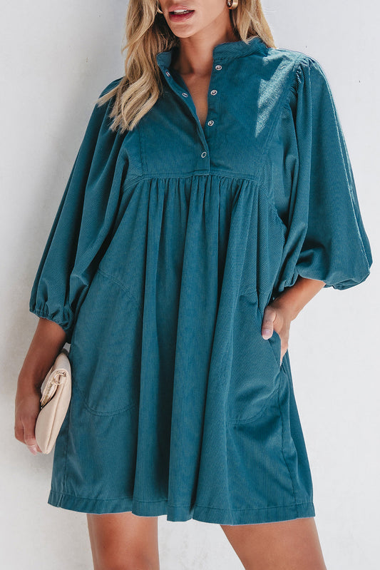 Teal corduroy babydoll dress with balloon sleeves, model holding a clutch