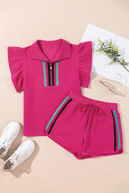 Hot pink quarter-zip top and striped shorts laid flat with sneakers