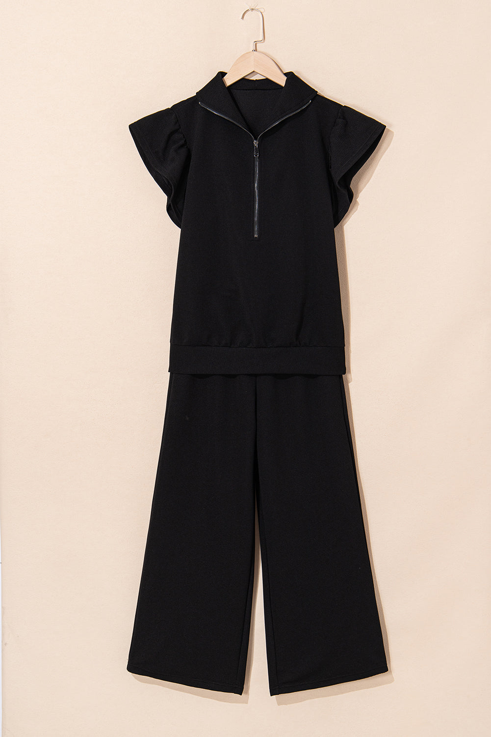 Black quarter-zip top and wide-leg pants on a hanger, front view