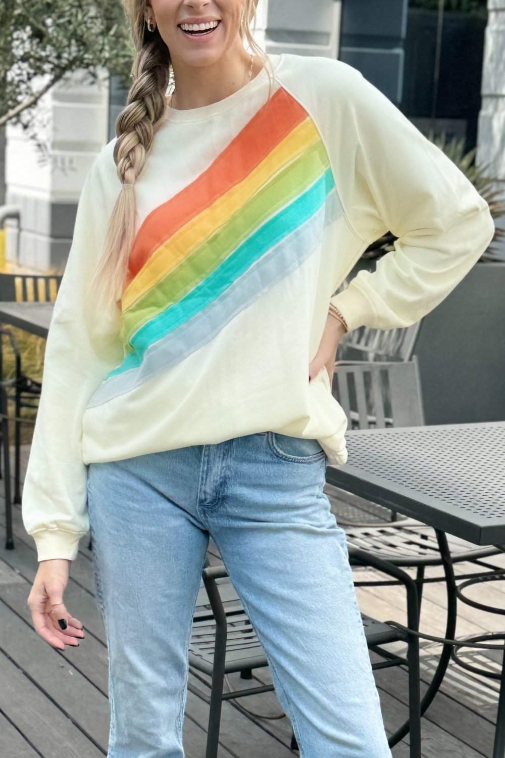 Cream sweatshirt with a diagonal rainbow stripe, worn with jeans