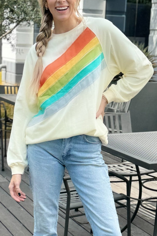 Cream sweatshirt with a diagonal rainbow stripe, worn with jeans