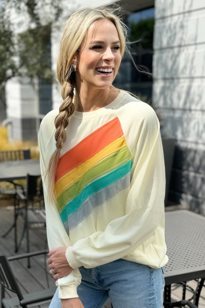 Close front view of the rainbow band on the cream sweatshirt