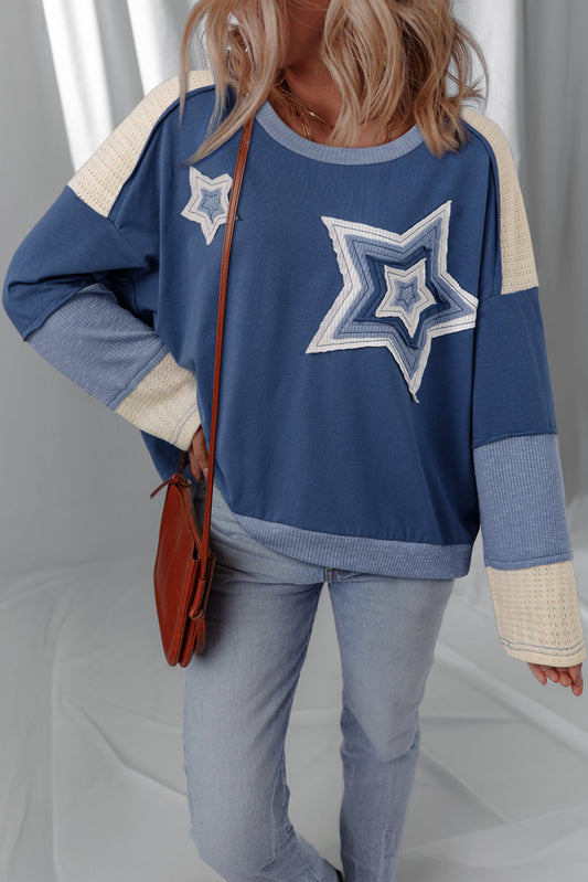 Dark blue knit top with layered star patches and cream shoulders, worn with jeans