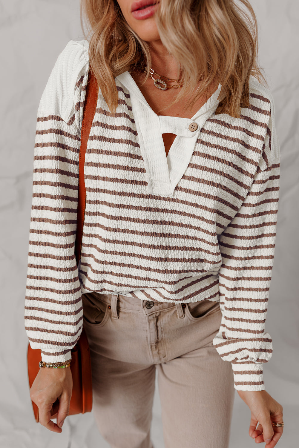 Brown and white striped hooded top with taupe pants and a cognac bag